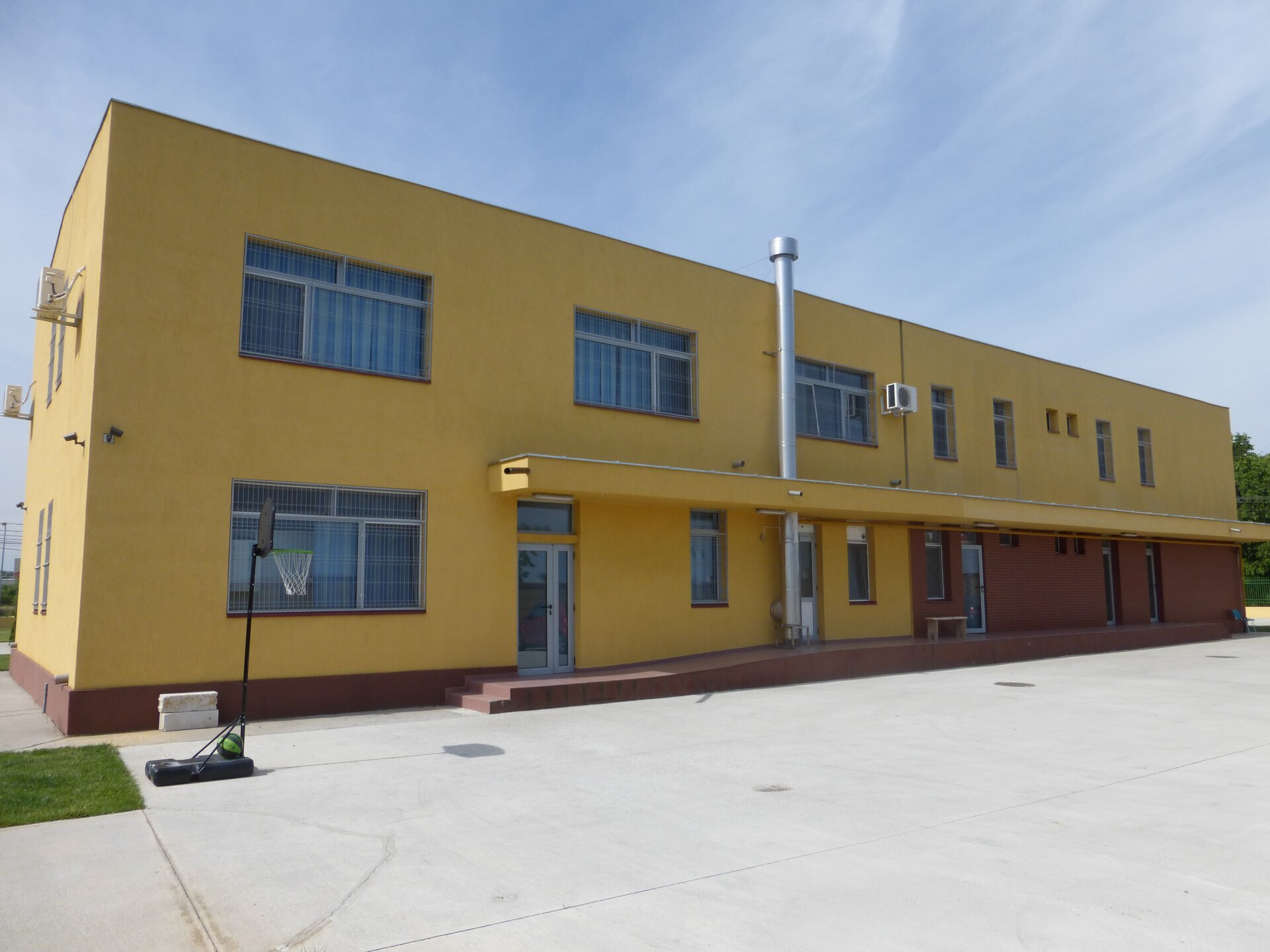 Fațadă laterală a Centrului de Reabilitare și Recuperare Neuropsihică Uverturii Sector 6, cu finisaj galben și soclu vișiniu și spațiu pavat de recreere în prim-plan, clădire P+1E finalizată în 2012, proiect PPAE
